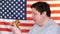 Fat man holding a piece of hamburger with an American flag background. Big guy wants fast food.