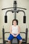 Fat thick little caucasian boy in white shirt sitting on exercise sport machine indoors