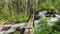 A fat tourist with a large backpack crosses a stormy mountain river in the forest on fastened logs