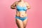 Fat woman in blue underwear on pink background, overweight female body