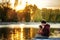 Father and 2 years old child play fishing on bank of lake in sunset time. Golden in sun light trees and water around. Father and
