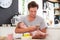 Father With Baby Daughter Checking Mobile Phone In Kitchen