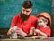 Father with beard and little son in classroom teaching to use tools, chalkboard on background. Boy, child in protective