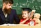 Father with beard, teacher teaches son, kid boy. Kid studies with teacher, near copybook, clock, toy. Teaching kid