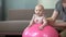 Father carefully holding baby girl on big ball, fitness exercises for infant