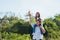 Father and carrying an excited girl on shoulders having fun and enjoying outdoor lifestyle together playing aircraft toy