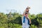 Father and carrying an excited girl on shoulders having fun and enjoying outdoor lifestyle together playing aircraft toy