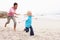 Father Chasing Daughter Along Winter Beach