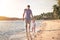 Father and child walking together on the beach coast during sunset with shining sea on background