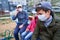 Father and children sitting on a bench on playground near high-rise buildings with apartments, a medical mask on their faces