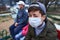 Father and children sitting on a bench on playground near high-rise buildings with apartments, a medical mask on their faces