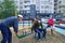 Father and children sitting on a seesaw on playground near high-rise buildings with apartments, a medical mask on their faces