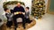 Father and children with twin boys exchange gifts and laugh in living room with fireplace and tall Christmas tree