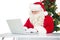 Father christmas using his laptop near christmas tree