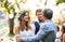 A father congratulating bride and groom at wedding reception in the backyard.