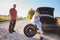 Father and daughter changing broken tire during summer rural road trip.