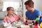 Father With Daughter Sitting At Table Decorating Eggs For Easter At Home