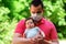 Father in facial mask holding in arms little baby daughter in summer day. Green leaves in background. Parenting during quarantine