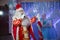 Father Frost speaks with a microphone . Santa Claus is singing Christmas songs against . Man in Santa Claus suit posing with