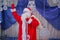 Father Frost speaks with a microphone . Santa Claus is singing Christmas songs against . Man in Santa Claus suit posing with