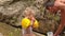 Father Gives Apple to Little Blond Girl in Arm-hands by Rocks