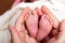 Father hands holding cute beautiful caucasian newborn baby boy little pink feet, one week old in white blanket. Concept