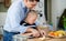 Father with happy down syndrome son indoors in kitchen, chopping fruit.