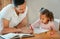 Father helping his daughter with her homework. Dad teaching daughter to read and write during homeschool class. Little