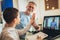 Father helps his son with home work. Boy in video conference with teacher on laptop at home