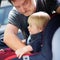 Father helps his toddler son to fasten belt on car seat