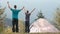 Father and his child son walking near camping tent with raised hands while hiking together in summer mountains. Active family trav