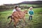 A father and his toddler children with a goat outside in spring nature.