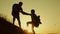 Father holds out his hand helping children climb mountain. Family of tourists with kids traveling at sunset. dad