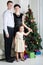 Father, mother and daughter stand near Christmas tree