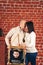 Father and mother kiss, and son peeks out of an improvised house in studio on background of brick wall. Copy space.