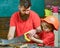 Father, parent with beard teaching little son to sawing with sharp handsaw, carpenter crafts. Boy, child busy in