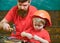 Father, parent with beard teaching little son to use hobnails and hammer. Boy, child busy in protective helmet learning