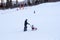 Father rolls his daughter on a sled on the mountainside against the background of the ski lift and the forest