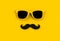 Father`s day concept. Hipster yellow sunglasses and funny moustache on yellow background