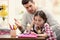 Father scolding his daughter while helping with homework at table