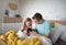 Father setting alarm clock with his little daughter with Down syndrome in bed at home.