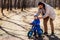 Father setting a cap to his toddler son in blue jumpsuit in the park. The child is sitting on a blue balance bike