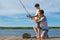 Father shows his son on the pier how to hold a fishing rod to catch fish, against a beautiful landscape