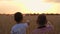 A father shows his son to a combine harvester that is harvesting wheat. Family business, happy family at sunset