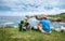 Father and son backpackers rest on the rocky sea side