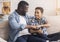 Father And Son Bumping Fists Sitting On Couch At Home