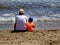 Father and son chatting at the seashore on a sandy beach on summer vacation