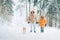 Father and son dressed in Warm Hooded Casual Parka Jacket Outerwear walking in snowy forest with his beagle dog in pine forest.