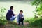 Father with son fishing at river bank, summer outdoor. Man and young boy standing at river bank with rod and fishing. Family