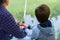 Father with son fishing at river bank, summer outdoor. Man and young boy standing at river bank with rod and fishing. Family